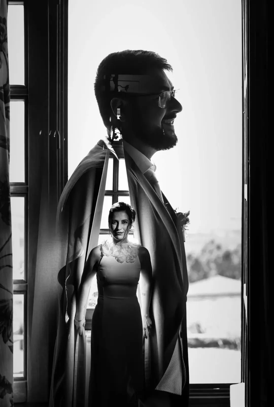 Retrato en blanco y negro que combina doble exposición, con la silueta del novio con gafas y barba a contraluz junto a una ventana superpuesta a la imagen de la novia sonriendo en un vestido sencillo.